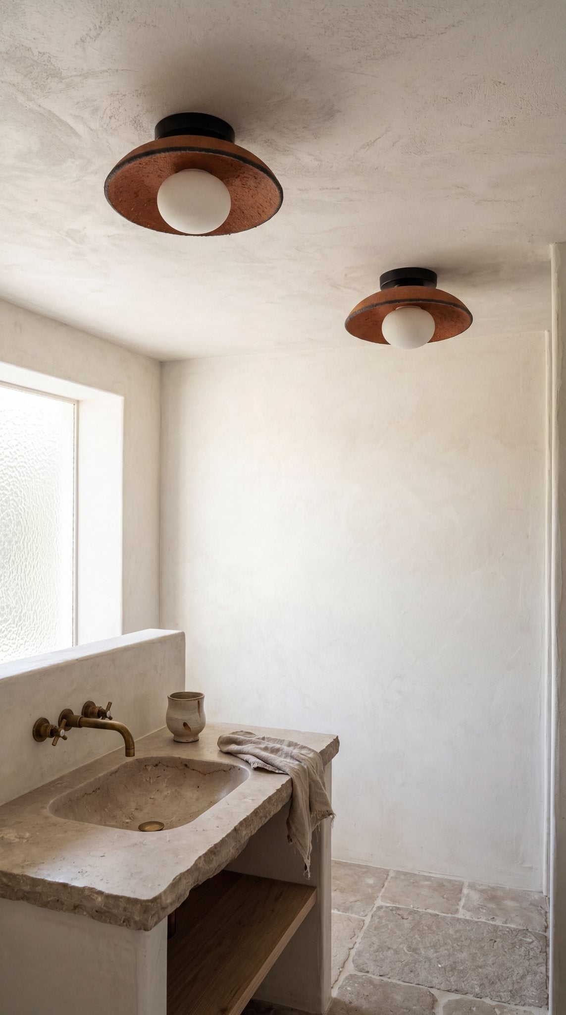 Two Ember terracotta ceramic flush mount ceiling lights in a plaster bathroom with a stone sink
