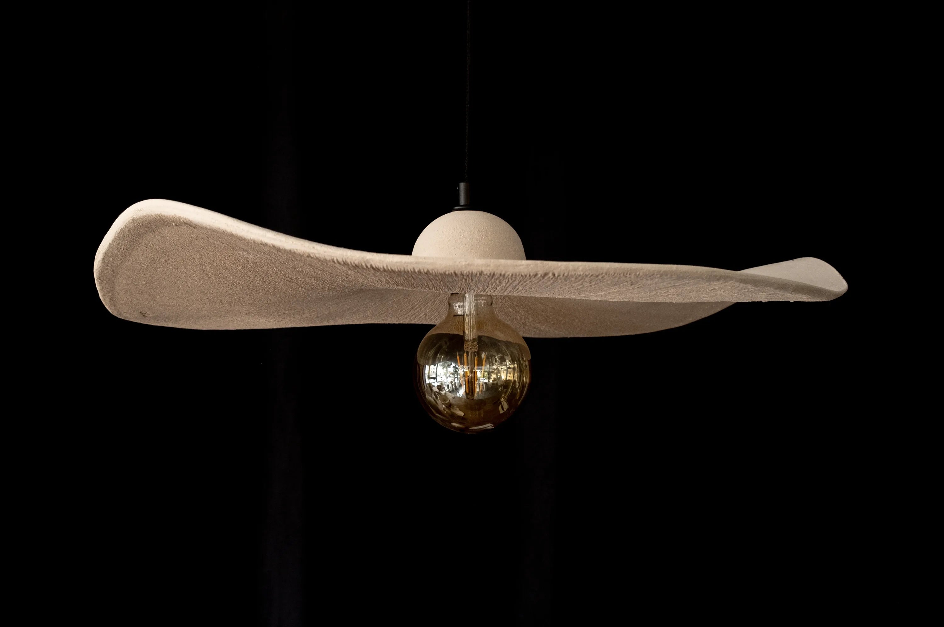 Wide, wavy-brimmed sand-coloured ceramic pendant with an amber globe bulb