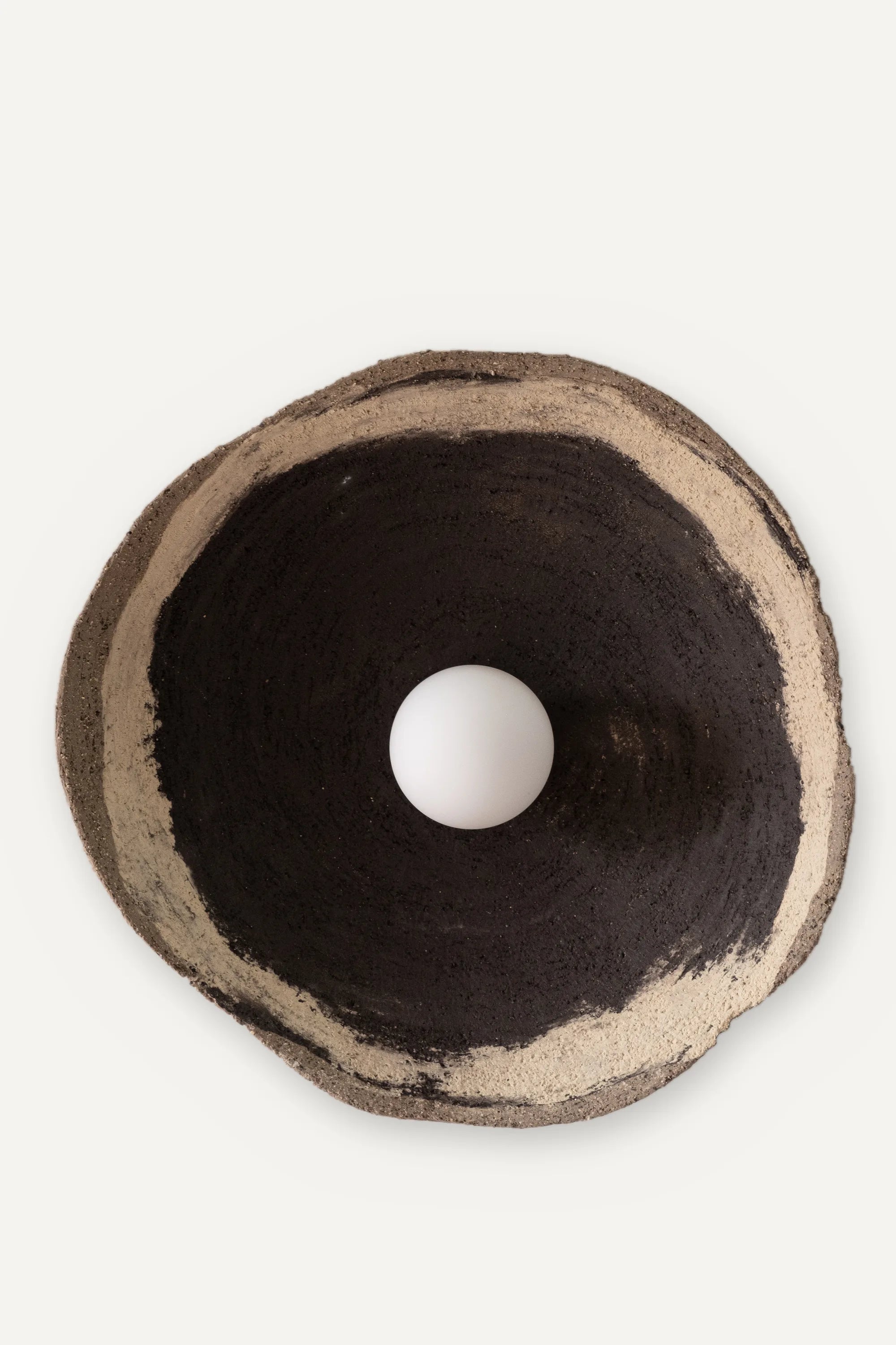 Round hand-built stoneware wall sconce with a sand-coloured rim, dark interior and white opal globe